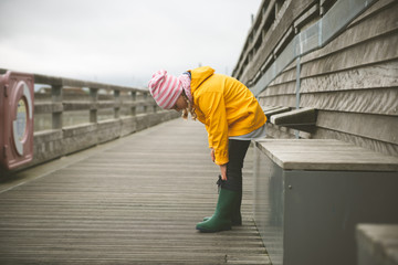 Portrait of little girl in yellow jacket on wooden pier at rainy weather