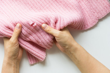 Woman hands holding knitted thing with hole made by moth