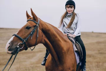 Foto op Canvas First lessons of horseback riding. Young beautiful girl riding a horse in a field. © Олег Кошевський