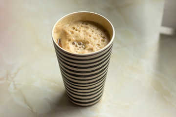 Woman is holding a bamboo travel mug with foamy coffee and soy/soya milk. Stripey coffee cup on the counter