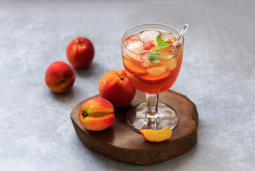 Glass of Peach Iced Tea with mint, sliced peaches and ice cubes on gray concrete background with copy space
