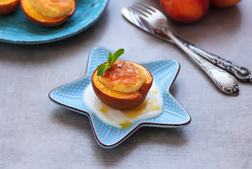 Stuffed baked peaches with cream cheese, honey, mint and yogurt on a plate on concrete background