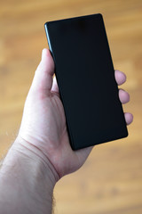 a man's hand holding a phone with a dark screen against a wooden defocused structure