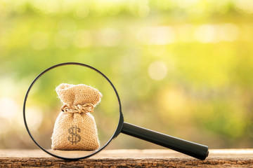 Magnifying glass with searching for money bag put on the wood on bokeh background, Loan and find...