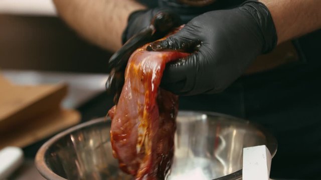 Professional chef marinating meat in a metal bowl in the kitchen of a fancy restaurant