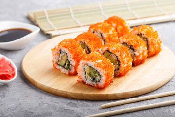 Japanese maki sushi rolls with flying fish roe on wooden board on a gray concrete background. Side view