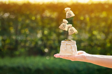 Women hand hold a coin pot and money bags and dropping on the top in the public park for loans to planned investment is together in the future concept.