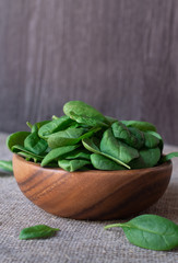 fresh green spinach leafs in a wooden bowl, isolated on wooden background