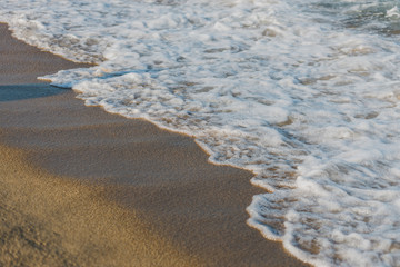 Close-up of a wave hitting a beach in warm sunset light