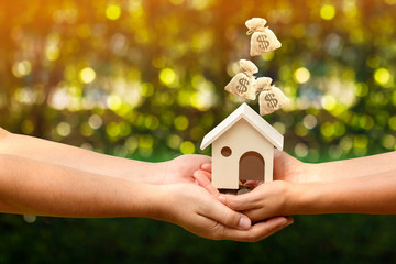 Man and woman hand hold a home model and coin and drop money bag presenting to each other in the...