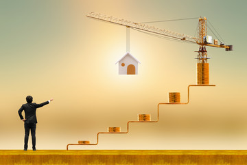 Businessman is working with stack coin with grow value on golden steps and tower crane with build house on sunlight background, Saving money and loan for construction real estate and home concept.