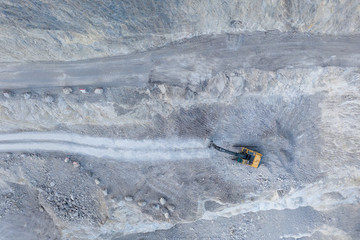 grey stone quarry pit from aerial bird's eye view with heavy shovel excavator