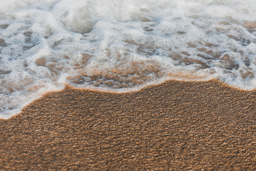 Close-up of a wave hitting a beach in warm sunset light