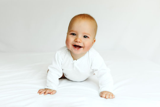 Beautiful happy baby smiling in white on the bed.