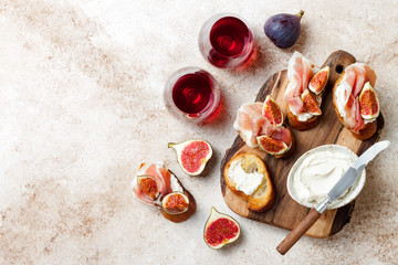 Obraz na płótnie Canvas Crostini with prosciutto, cream cheese and figs on wooden board. Appetizers, antipasti snacks and red wine in glasses. Authentic traditional spanish tapas set. Light beige background. Top view