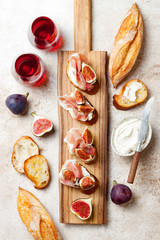 Crostini with prosciutto, cream cheese and figs on wooden board. Appetizers, antipasti snacks and red wine in glasses. Authentic traditional spanish tapas set. Light beige background. Top view