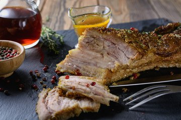 Appetizing baked pork belly with streaks of fat and meat next to spices, peas of pepper, sprigs of thyme and sauce