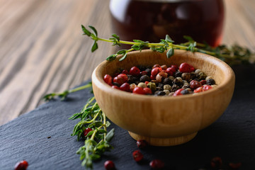 A mix of different  peas of peppers in red, black, white, green in a wooden bowl next to sprigs of thyme and wine vinegar are ready for cooking eat