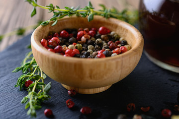 A mix of different  peas of peppers in red, black, white, green in a wooden bowl next to sprigs of thyme and wine vinegar are ready for cooking eat, closeup