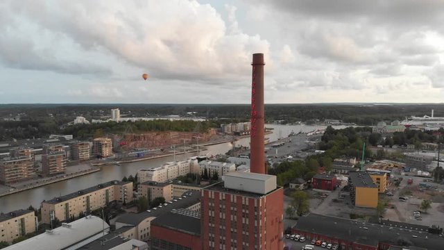 Vertical movement aerial in a European city, overlooking a factory chimney, hot air balloon in the background