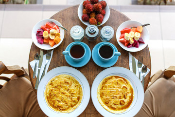 Top view, table setting. Balinese tropical breakfast of fruit, coffee and scrambled eggs and banana pancake for two. on the street near the pool