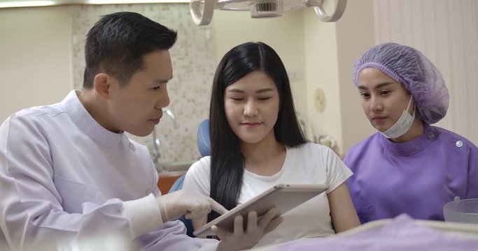 Dentist showing teeth x-ray image on digital tablet to patient. Dentist and patient choosing treatment in a consultation with medical equipment in the background.