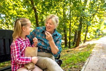 Fototapeta na wymiar Grandmother and granddaughter having fun while eating popcorn in park