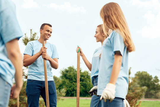 Volunteering. Young people volunteers outdoors planting trees talking looking at each other happy close-up