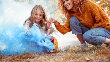 Young adult mother and daughter looking at carved pumpkin with smoke