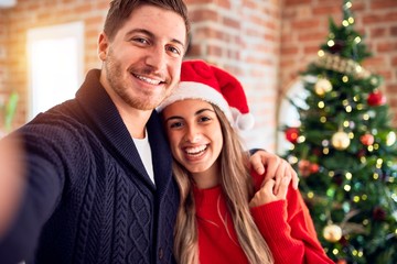 Young beautiful couple smiling happy and confident. Standing make selfie by camera around christmas tree at home