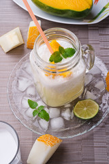 fresh vegetarian tropical melon cocktail with coconut milk and mango. served in transporant cup with ice, fresh melon, mango, lime, melissa  and coconut milk on grey napkin.   close up