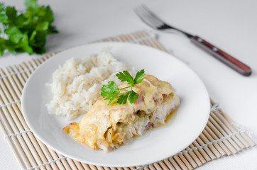 Baked fish with cheese, tomatoes and rice on a white plate. Sea catfish. close-up