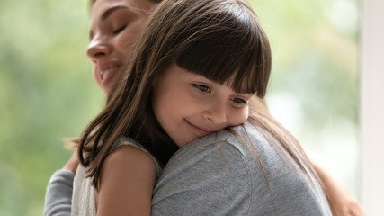 Happy little adopted kid girl put head on mothers shoulder.