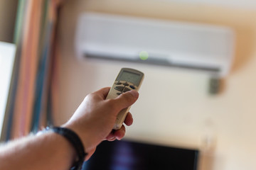In male hands of the remote control air conditioning in the hotel room. Cooling and airing in the hotel room. Close-up view of the use of some electrical appliances such as air conditioning.