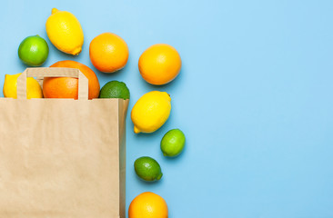Creative background with tropical fruits. Orange, lemon, lime, grapefruit drop out of paper bag on blue background. Flat lay top view copy space. Food concept, vitamin C, disease prevention, flu