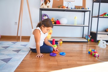 Adorable toddler playing building pyramid using hoops around lots of toys at kindergarten
