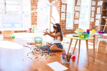 Adorable toddler playing with building blocks toy around lots of toys at kindergarten