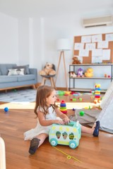 Adorable blonde toddler playing with car toy around lots of toys at kindergarten