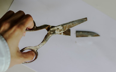 Woman's holding a pair of old broken scissors. Cutting the paper with rusty scissors. Point of view
