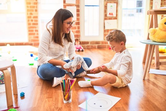 Beautiful teacher and toddler drawing using digital board around lots of toys at kindergarten