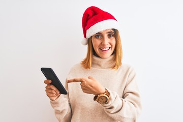 Beautiful redhead woman wearing christmas hat and using smartphone very happy pointing with hand and finger