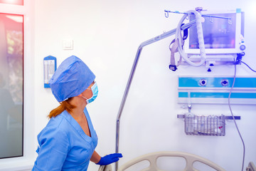 Nurse in blue medical clothes and mask is looking at the screen with health parameters on it. Medical chamber. First aid. Reanimation.