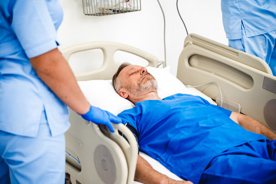 Seniour Male patient lying on a medical bed in hospital ward. Uncontious man in chamber. Blue medical clothes.