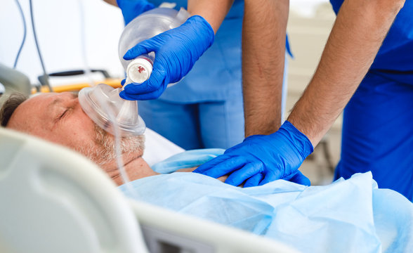 Doctors putting an oxygen mask on patient in hospital. First aid help. Reanimation room. Uncontious patient.