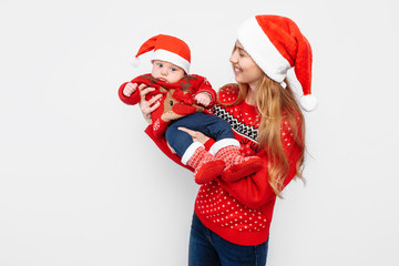 Young mother in santa hat with little baby in santa costume standing on white background