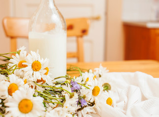 Obraz na płótnie Canvas Simply stylish wooden kitchen with bottle of milk and glass on table, summer flowers camomile, healthy foog moring concept close up