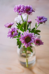 Pink and white flowers in a vintage school milk bottle being used as a vase on a wooden table