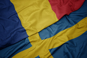 waving colorful flag of sweden and national flag of romania.
