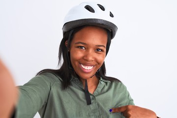 Young african american woman wearing bike helmet taking a selfie over isolated background with surprise face pointing finger to himself