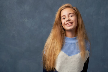 Teenage girl blonde in warm sweater isolated wall